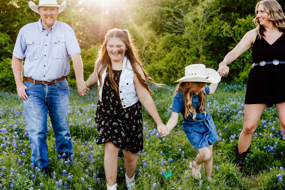 A family walks together holding hands in a meadow of bluebonnets at sunset.