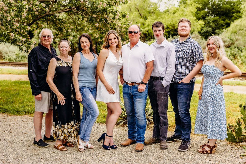 Group portrait of people standing together outdoors on a paved path with green trees in the background.