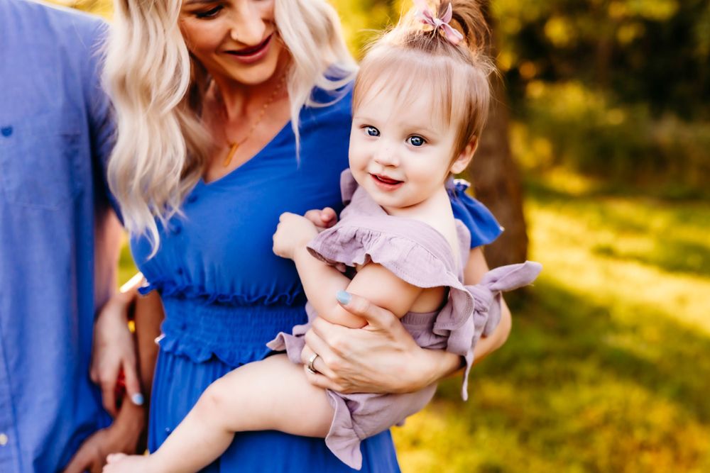 Close-up portrait of parent and child in blue and pink outfits against sunny natural backdrop.