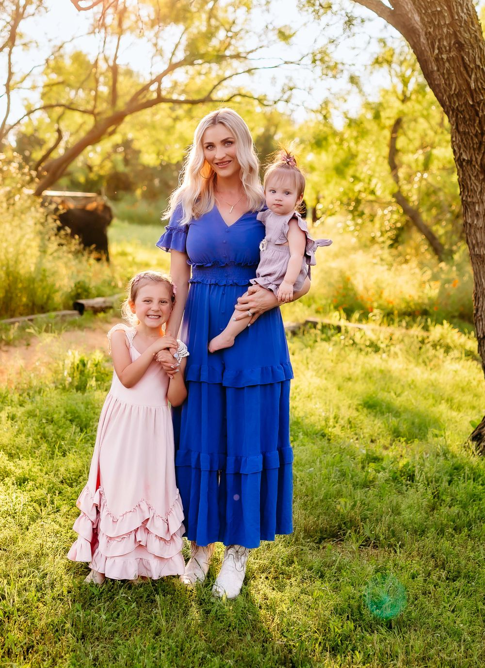 Mother and children portrait in a sunny garden setting wearing blue and pink dresses.