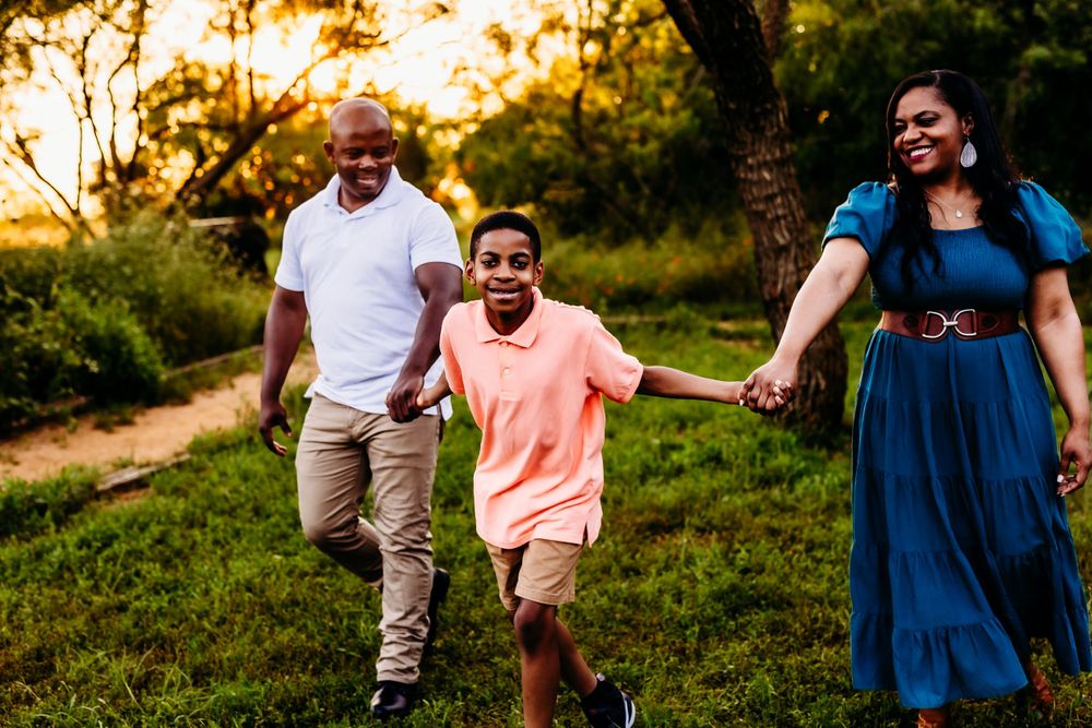 Family running and laughing together during golden hour in a grassy field.