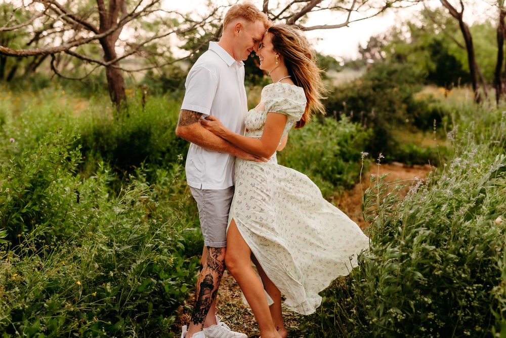 Romantic couple embracing in white outfits among wildflowers during sunset.