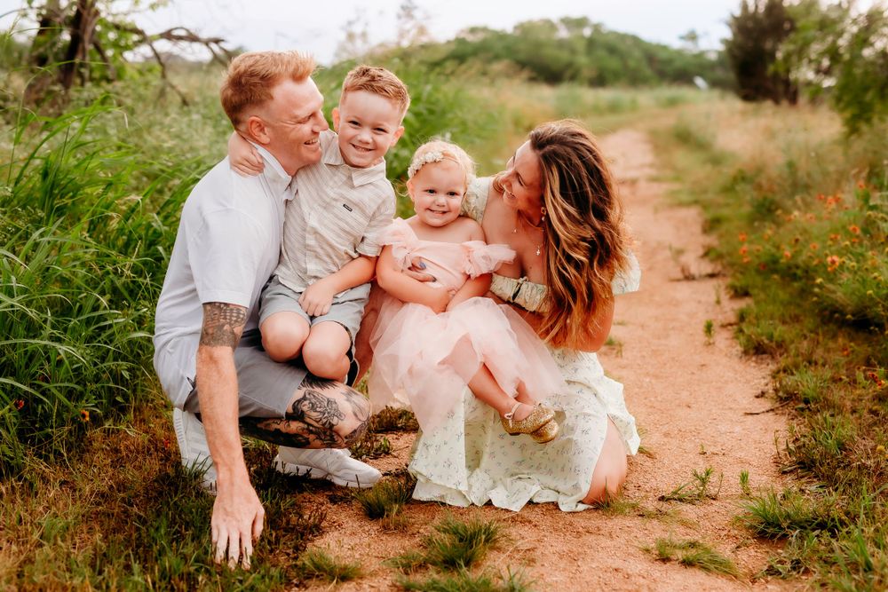 Family sitting together on a rustic dirt path surrounded by wild grasses during sunset.