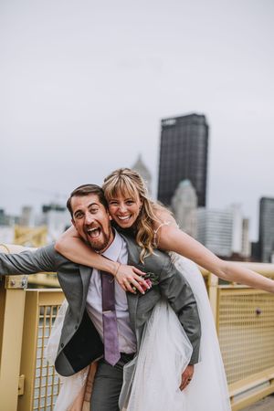 Joyful bride and groom posing on a yellow bridge with Pittsburgh city skyline in the background on their wedding day.