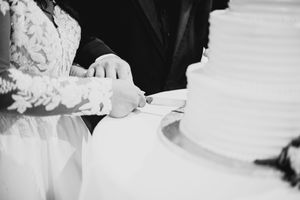 Black and white photo of bride and groom cutting their white wedding cake together.