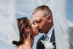 Bride and groom share a romantic kiss under a flowing white veil on their wedding day.