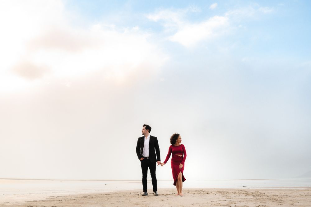 Couple walking along minimalist beach landscape under cloudy sky.
