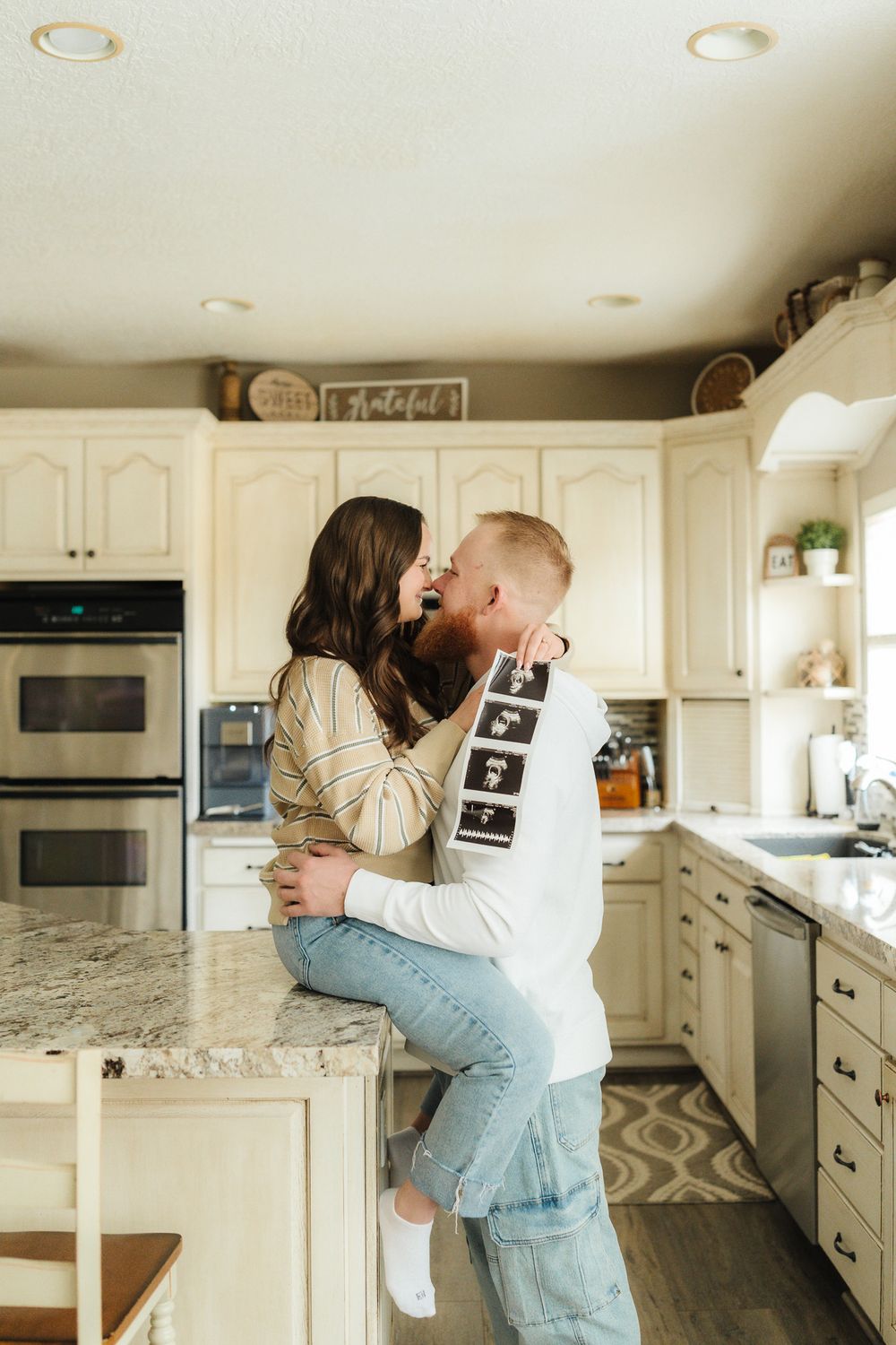 Couple embracing on kitchen counter holding ultrasound photos.