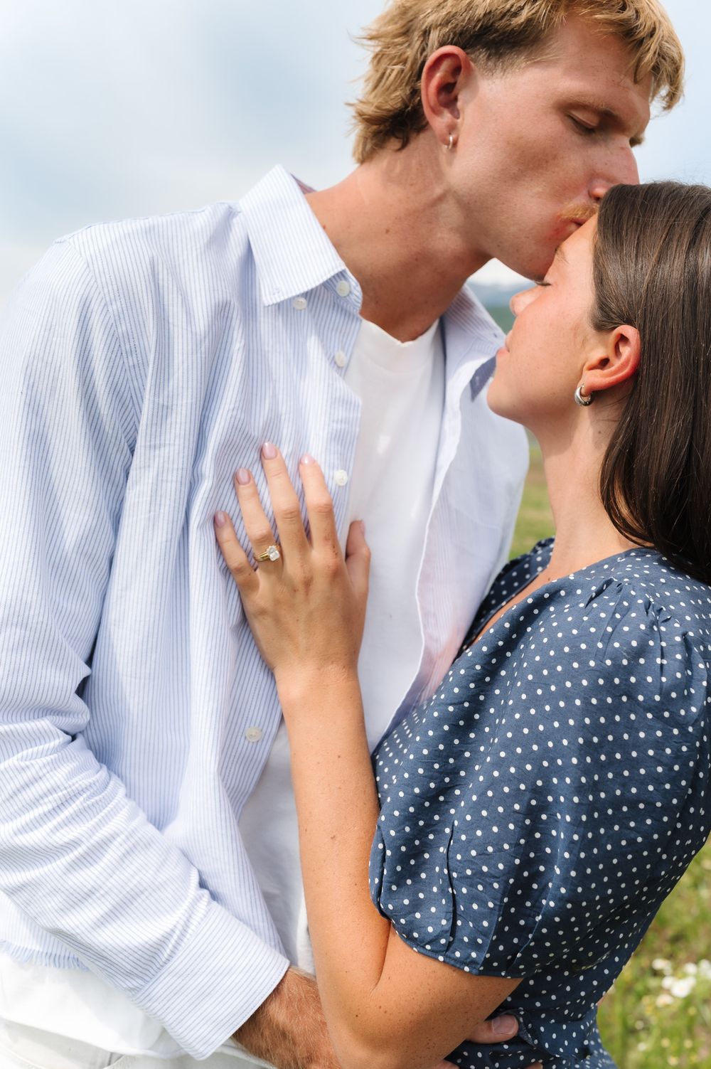 Romantic moment captured in a field with white and blue polka dot dress details.