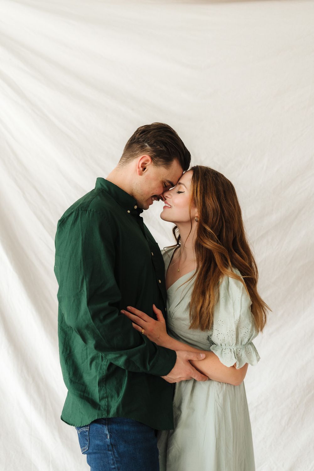 Couple embracing and sharing tender moments during a studio photoshoot with white backdrop.