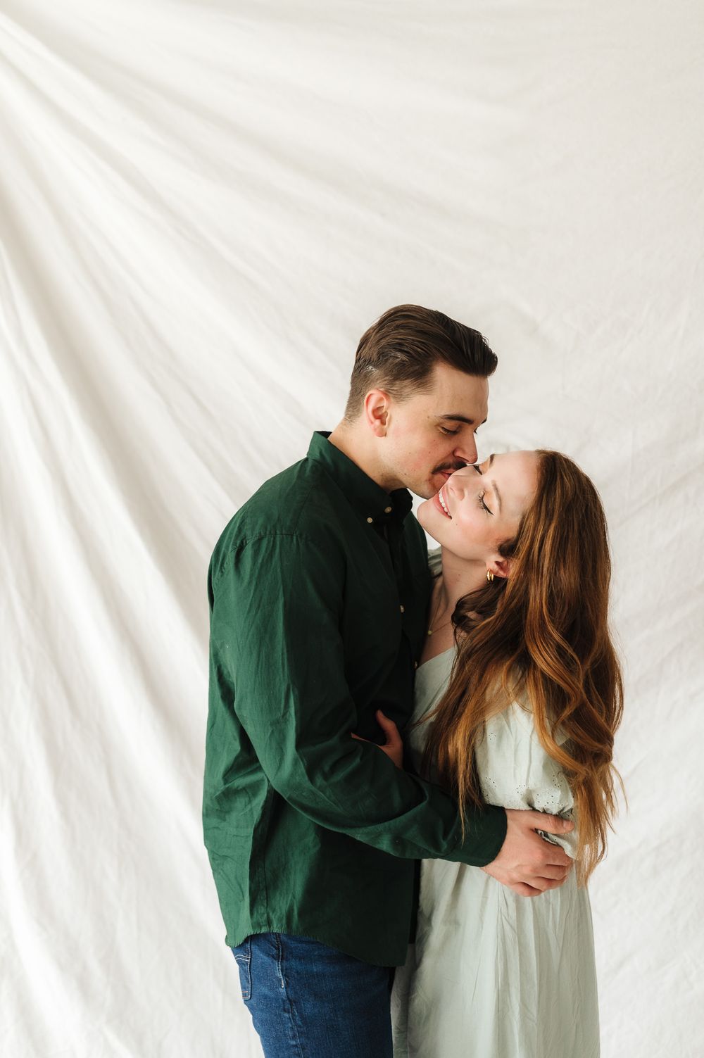 Romantic couple sharing intimate moments against a white backdrop in a studio setting.
