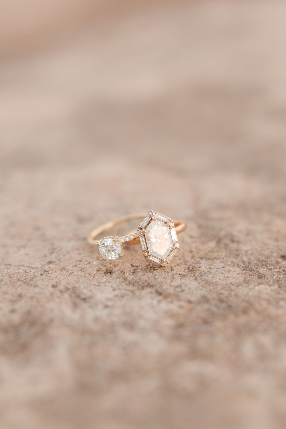Delicate rose gold engagement rings with diamonds displayed on a textured beige surface.