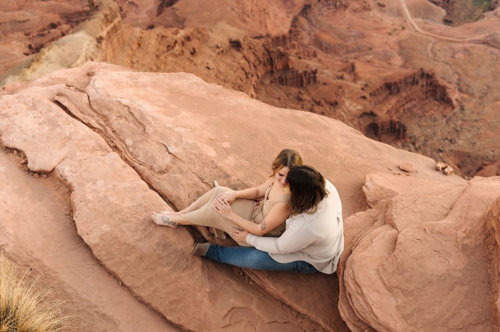 A couple poses together on red rock formations in a desert landscape during a photo session.