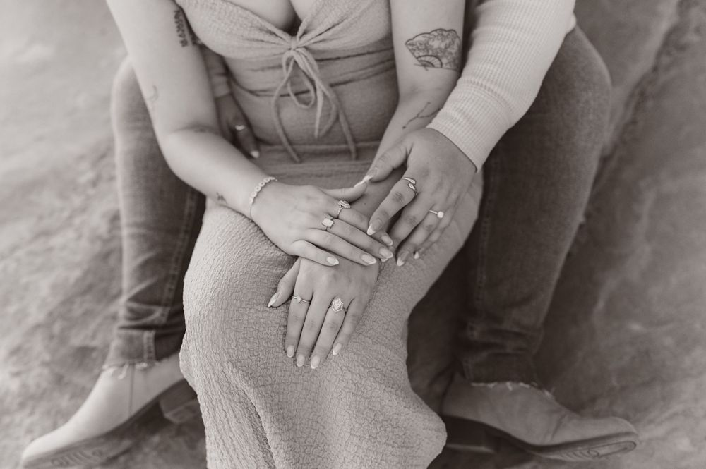 A couple embraces while sitting on red sandstone rocks in the desert.
