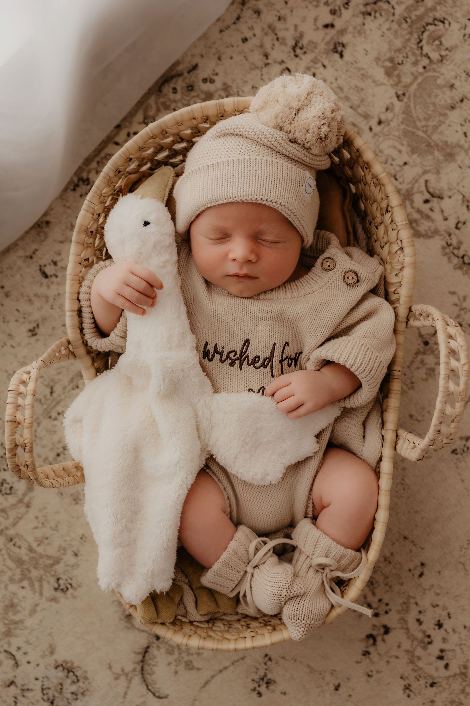 Sleeping newborn baby resting peacefully in a woven basket with knit blanket and sun decorative accent.
