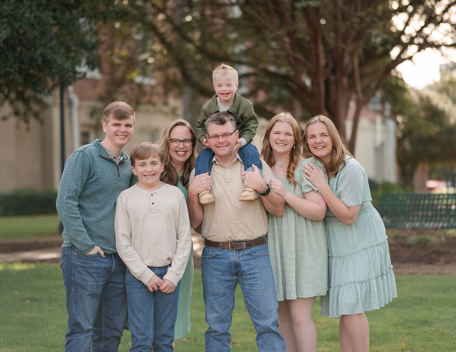 A family group poses together on fallen leaves with autumn foliage and lake in background.