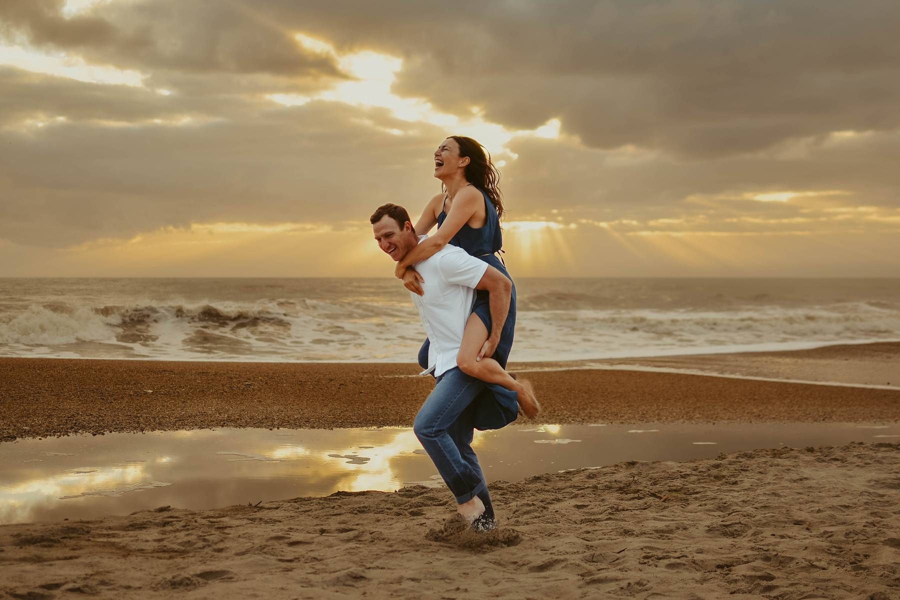 Romantic beach photoshoot with couple dancing in golden sunset light.
