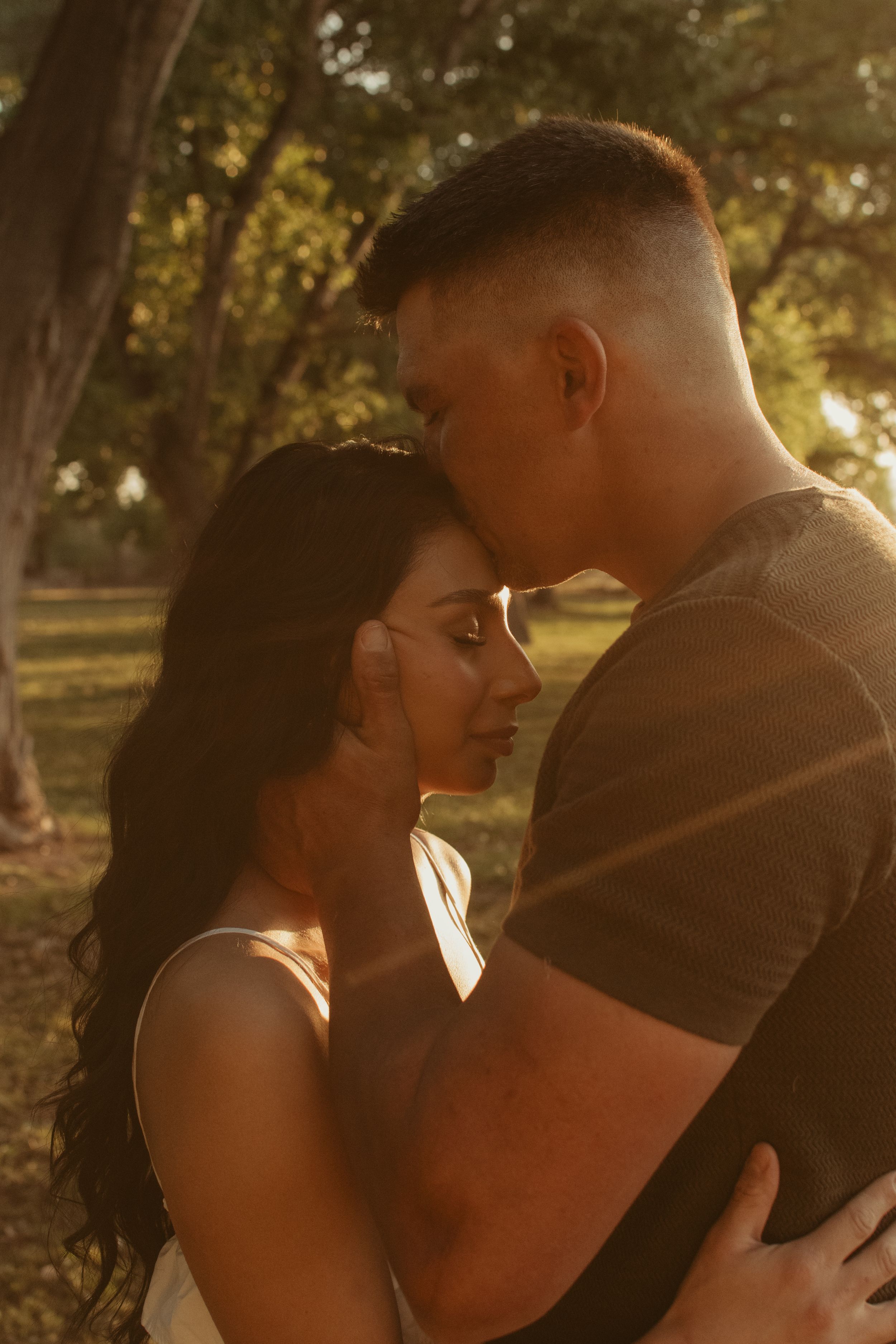 A romantic couple sharing a tender moment in golden sunlight filtering through trees.