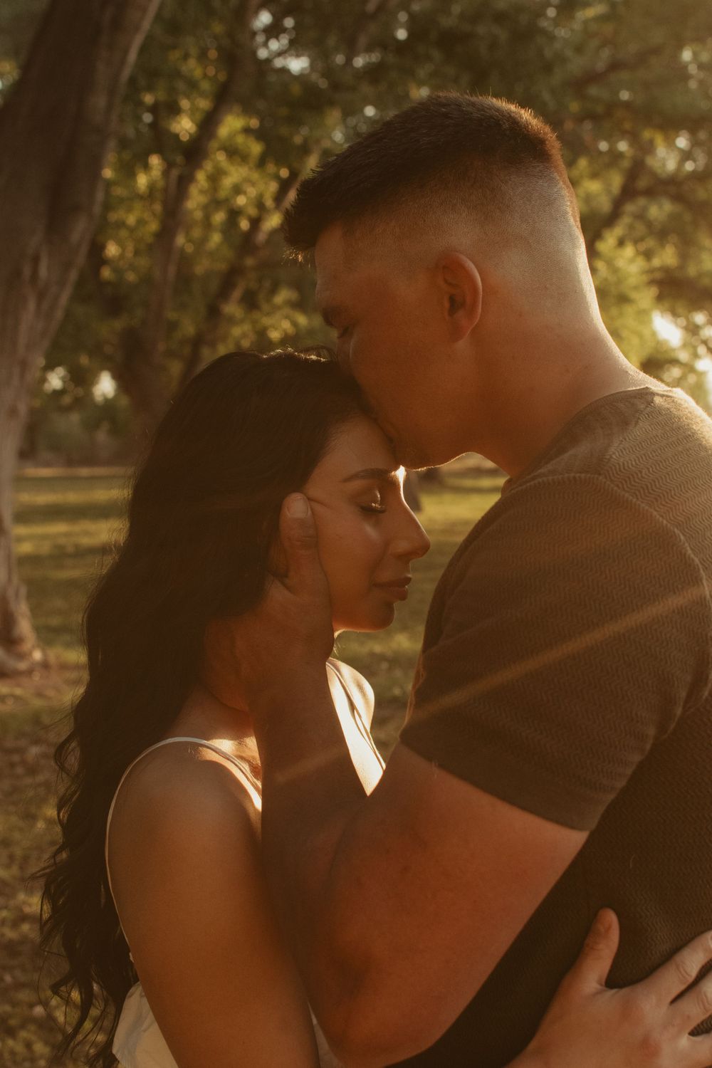 A romantic couple sharing a tender moment in golden sunlight filtering through trees.