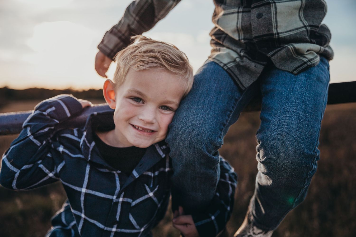 Candid outdoor family moment captured during sunset with denim and plaid clothing.