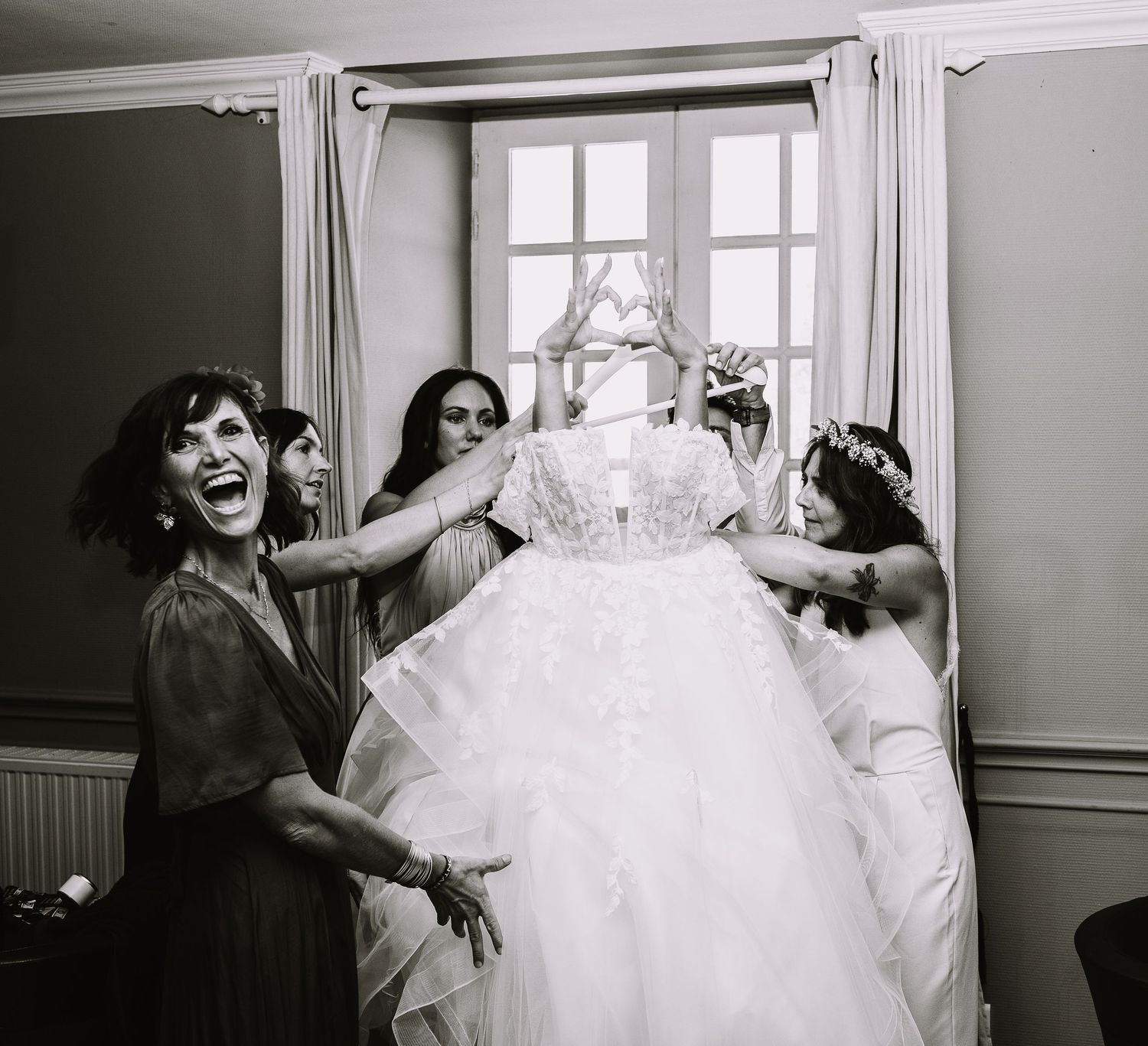 Témoins riant en soulevant la robe de mariée pendant les préparatifs, photo noir et blanc