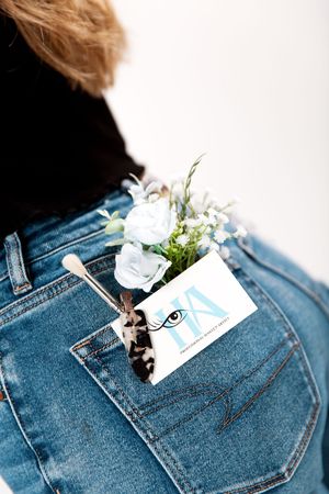 Artistic flatlay of beauty products and flowers tucked into denim pocket.
