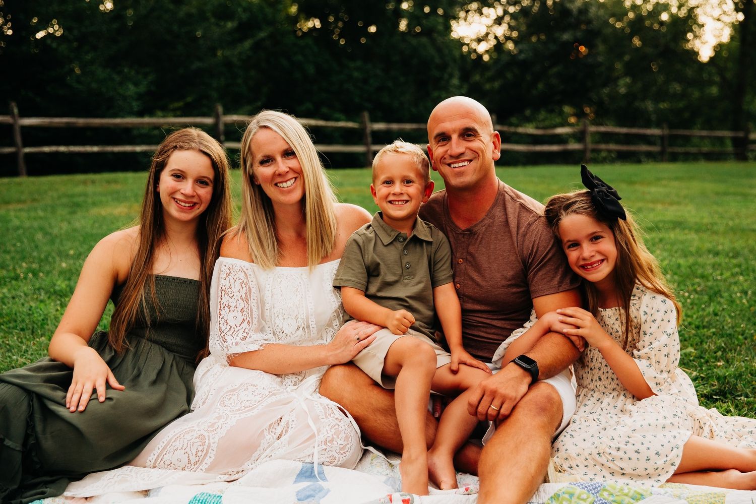 A casual outdoor family portrait on a blanket in a grassy field during summer.