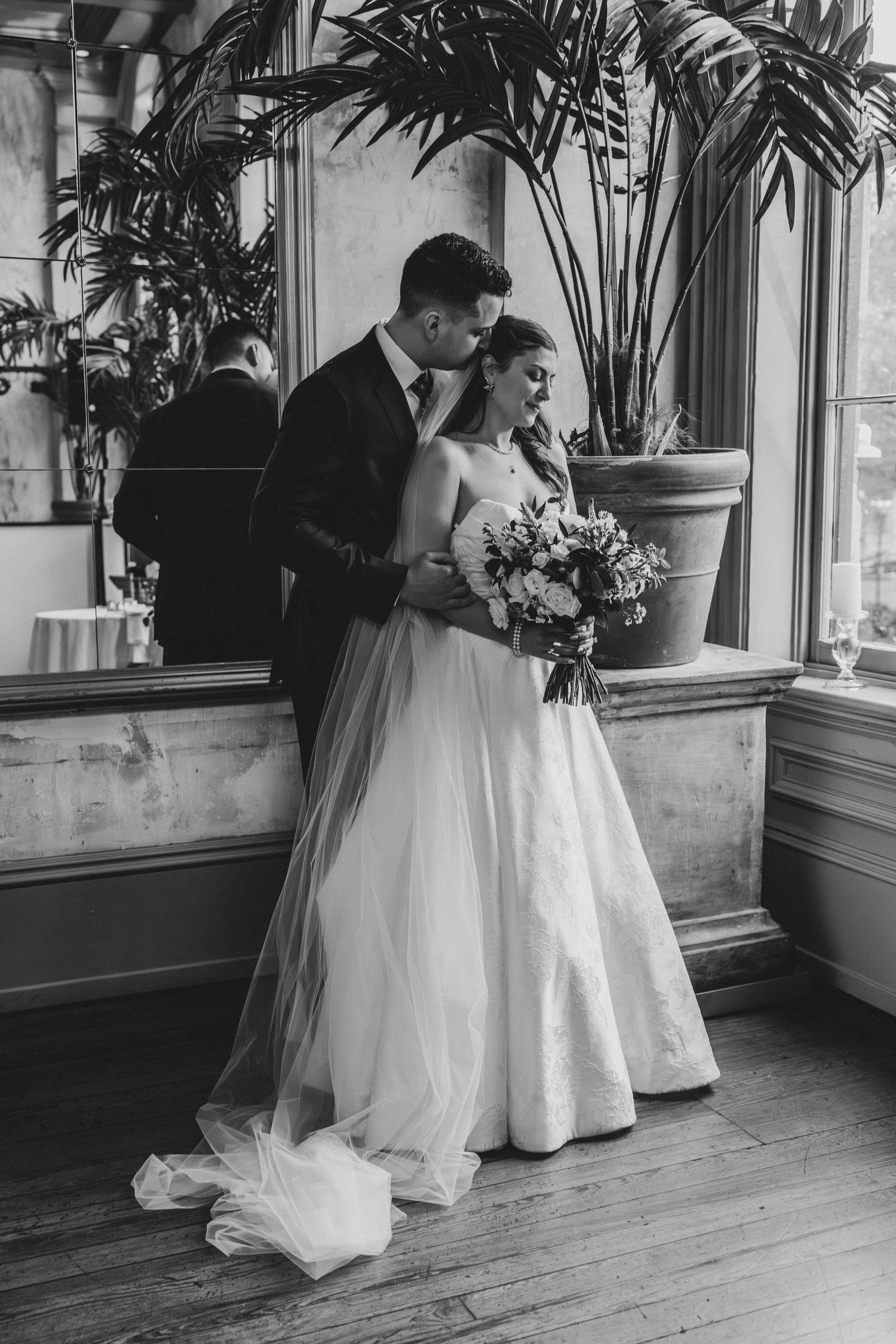 Black and white photo of a bride and groom sharing an intimate moment indoors, bride holding a bouquet in a ballgown.