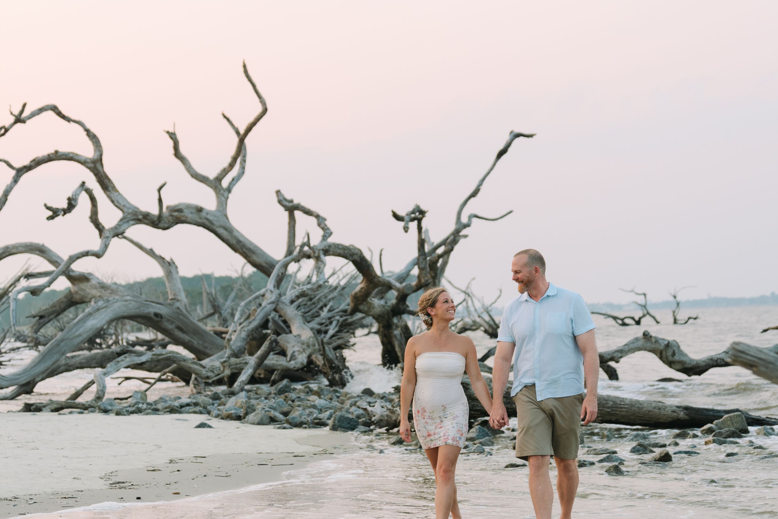 Wide view of Rachel and Bo among the driftwood at their Jekyll Island beach engagement session