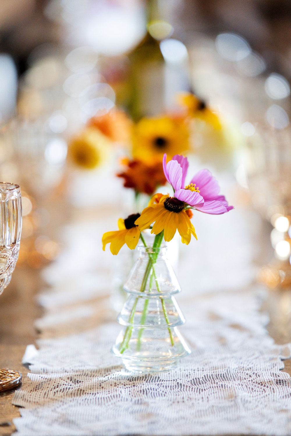 Close-up of homegrown pink cosmos and black-eyed Susan wildflowers in a ribbed glass bud vase for a rustic barn wedding reception.