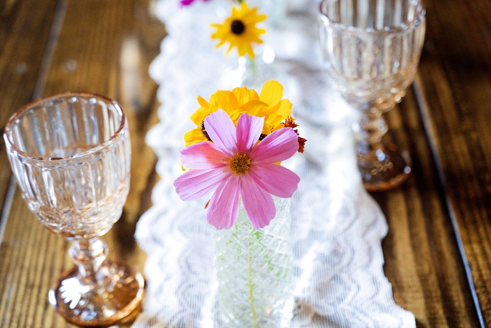 Overhead view of pink wildflower centerpieces and vintage amber glass chalices on dark wood tables at a Centennial Barn wedding.