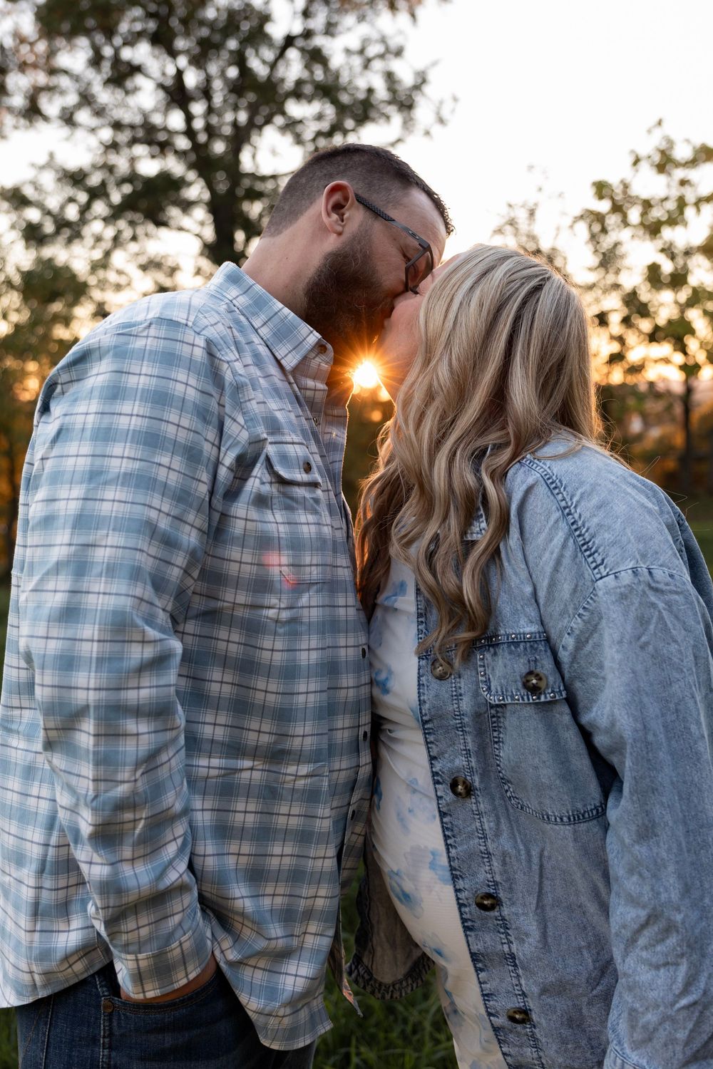 Couple kissing with sun rays beaming between them during a golden hour maternity session