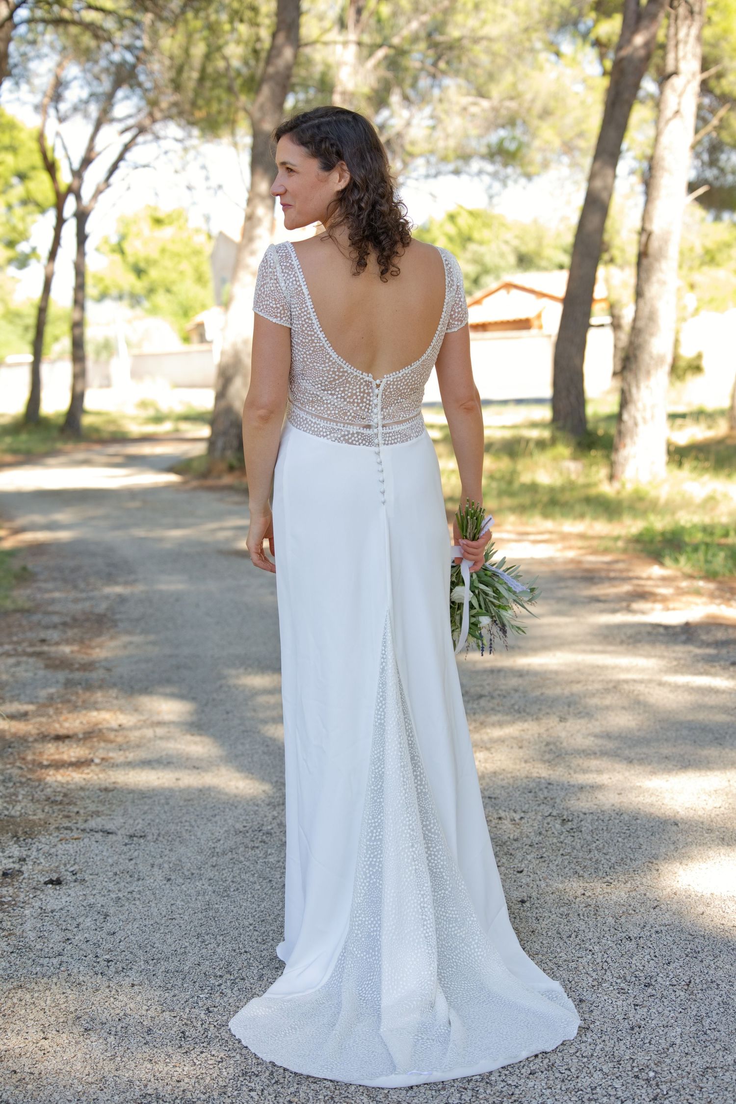 Augustine de dos, en robe de mariée et voile, pendant les portraits sous les pins.