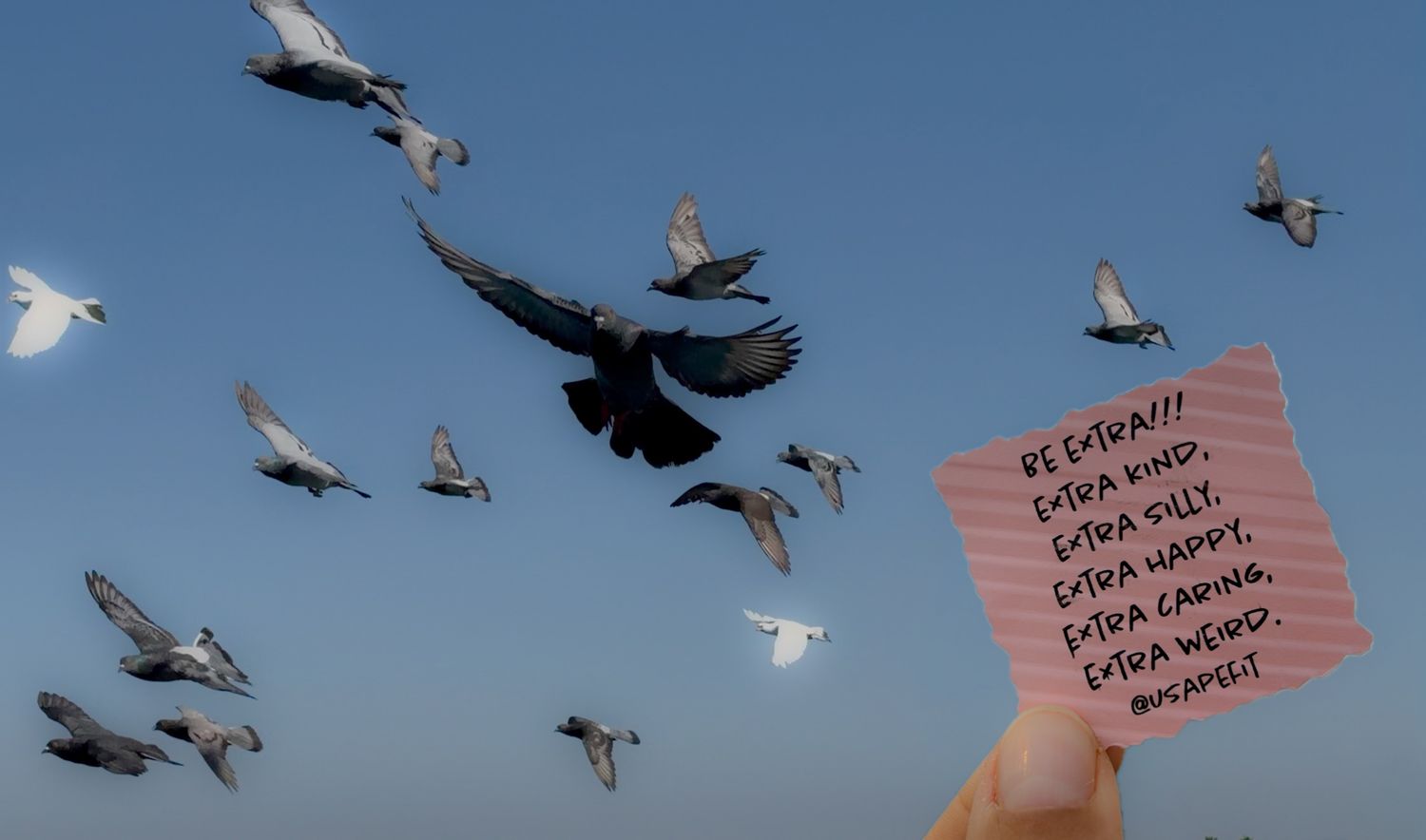 Hand holding a pink note with motivational text among flying birds against a blue sky.