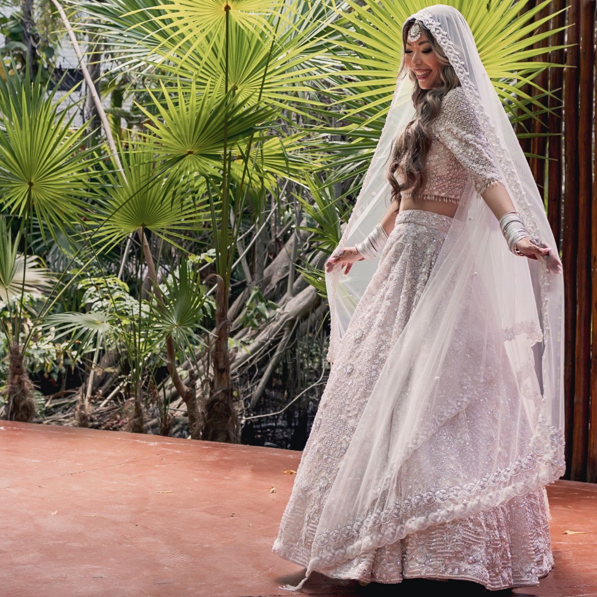 A joyful couple in traditional Indian wedding attire walks under a floral arch, surrounded by celebrating guests.
