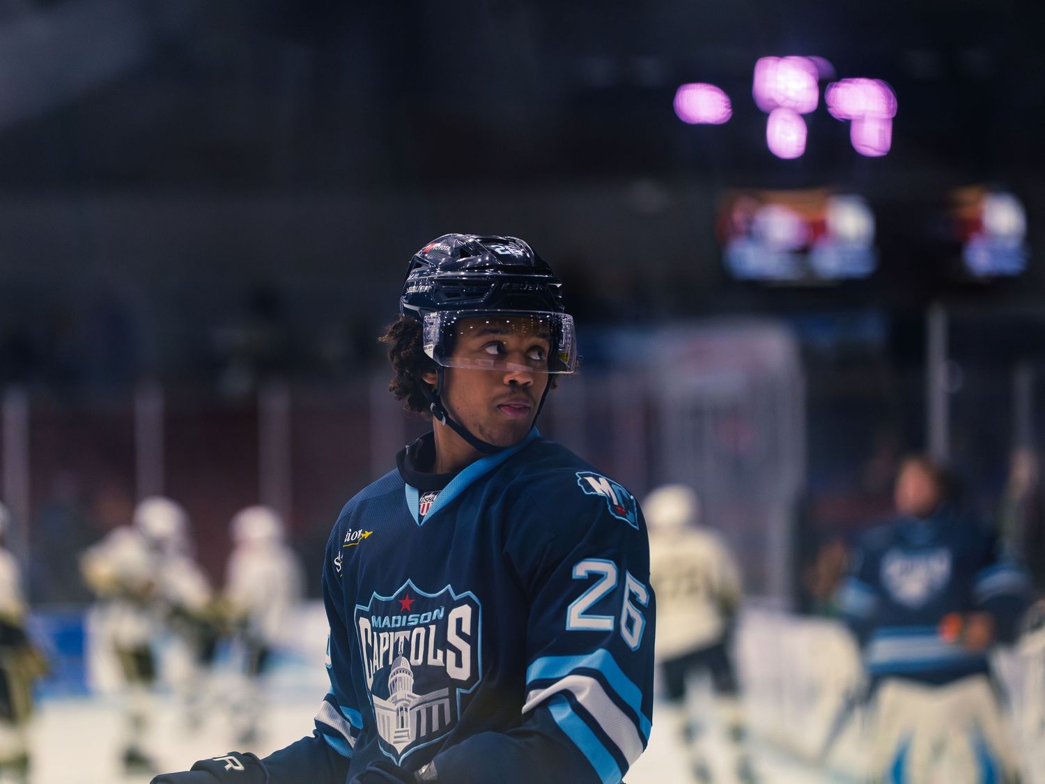 A Madison Capitols player in a navy number 26 jersey looks off to the side during warmups, the capitol-dome crest visible on his chest.