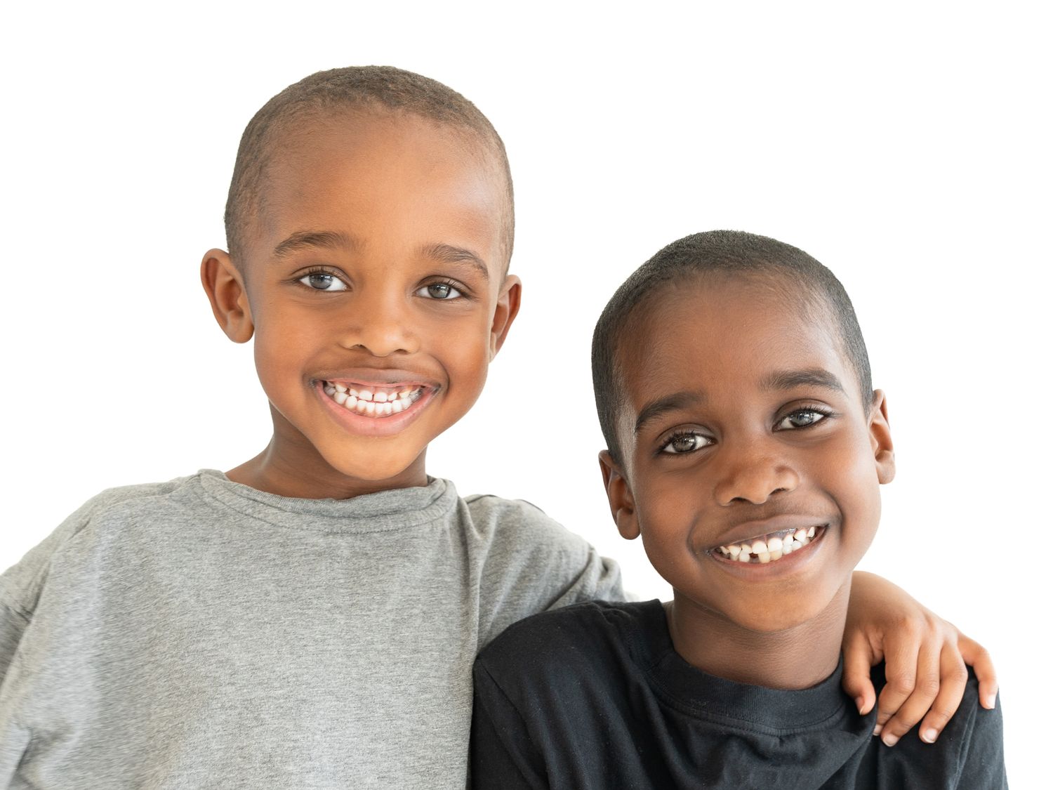 Two smiling children standing close together, one with an arm around the other’s shoulders, against a white background.