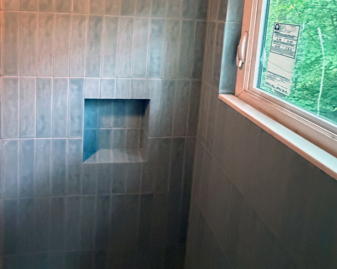 Gray tiled shower interior with recessed niche shelf and window, featuring vertical tile layout.