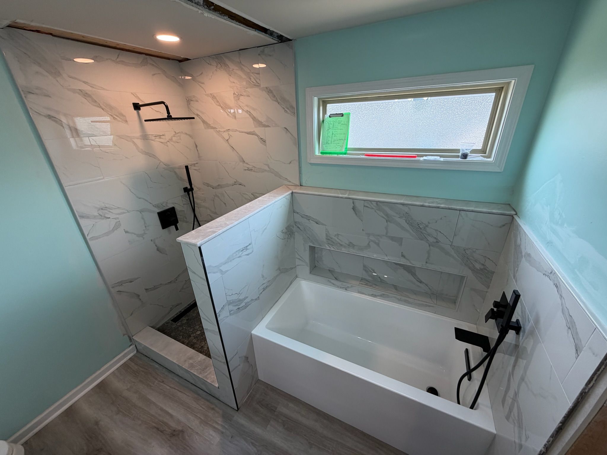 Completed bathroom renovation with marble tile, freestanding soaking tub, glass shower, and wood-look flooring.