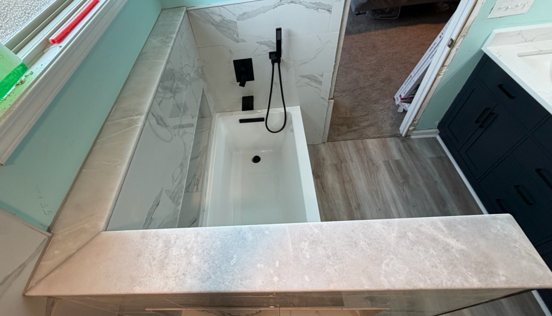 Overhead view of white marble tiled bathroom with freestanding soaking tub and black fixtures.