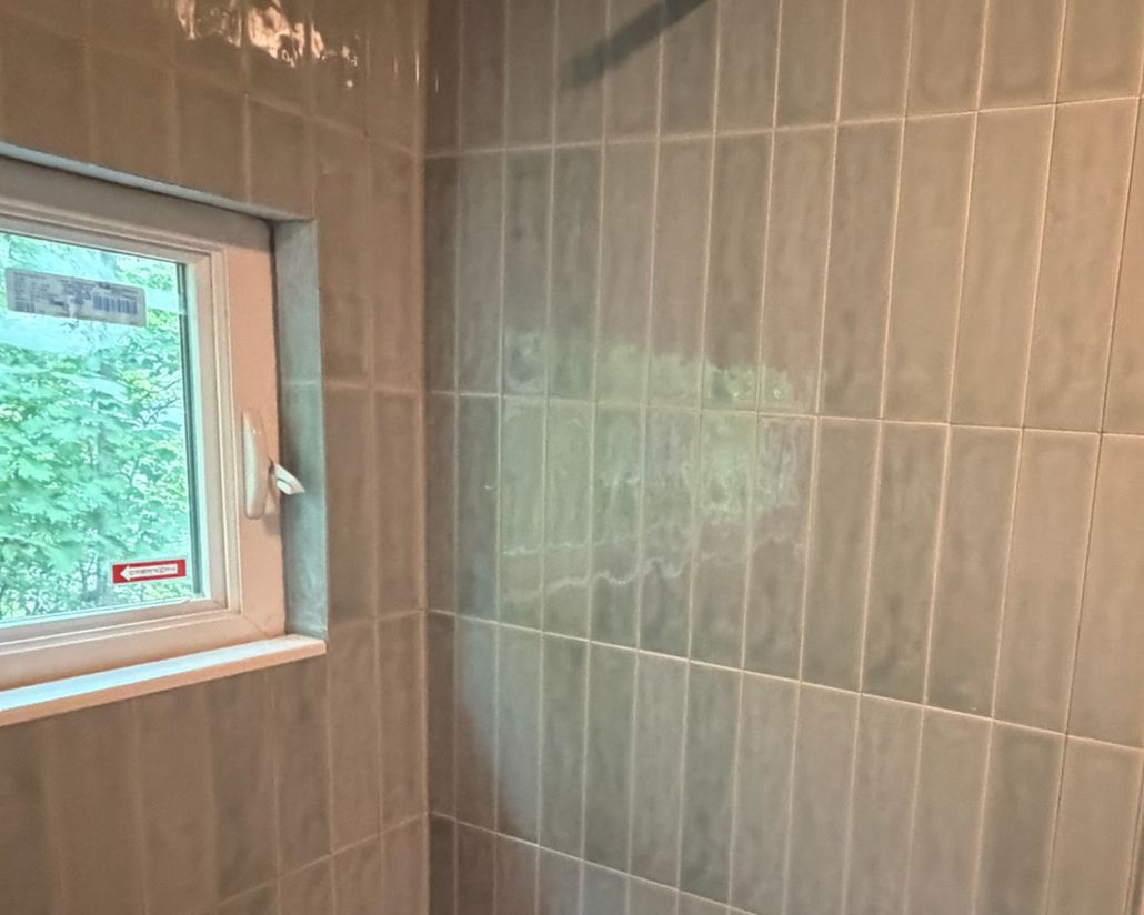Gray ceramic shower wall tiles with window, showing grout haze during bathroom renovation process.