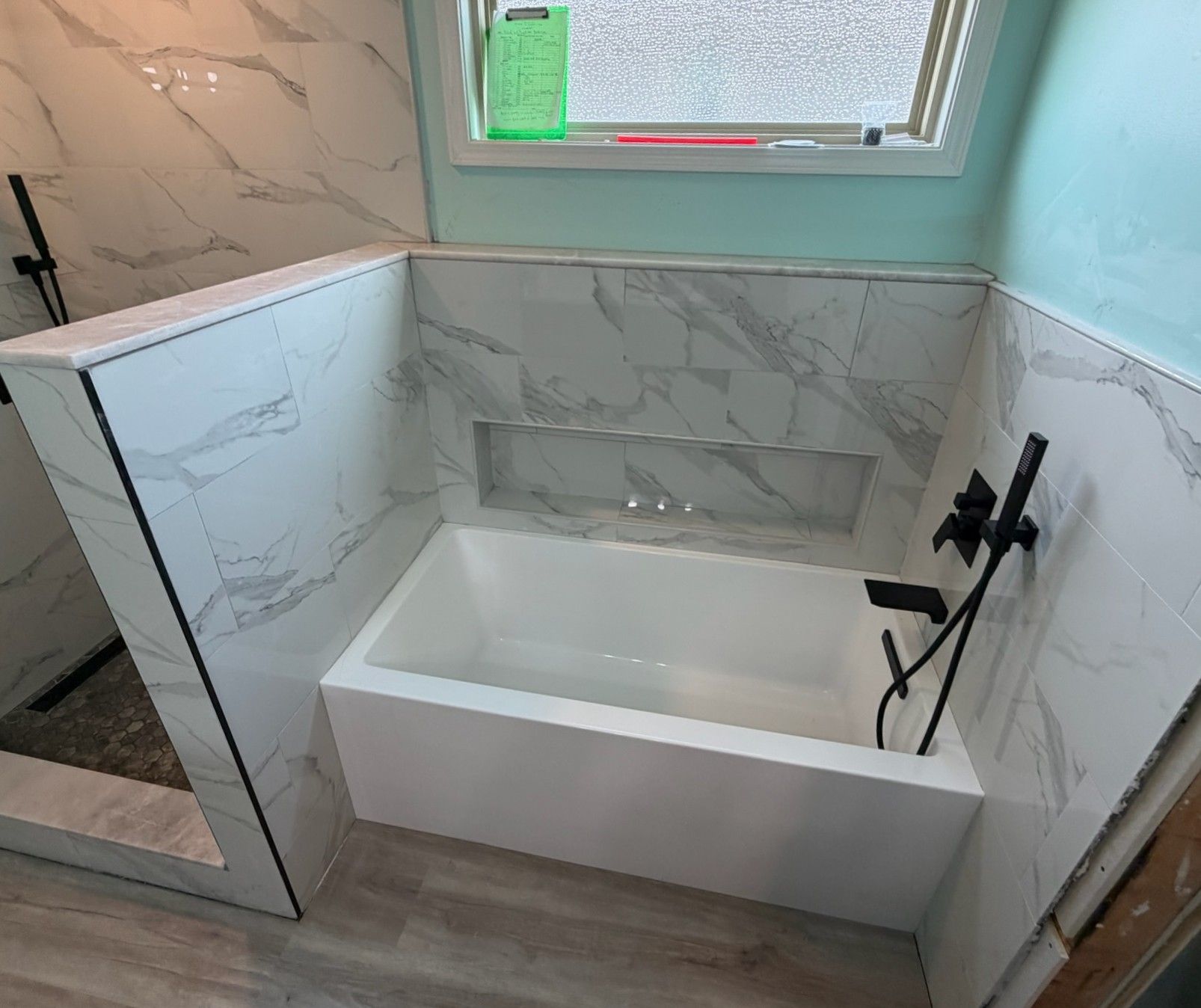 Elegant white marble tiled bathroom featuring freestanding tub, black fixtures, and glass shower partition.