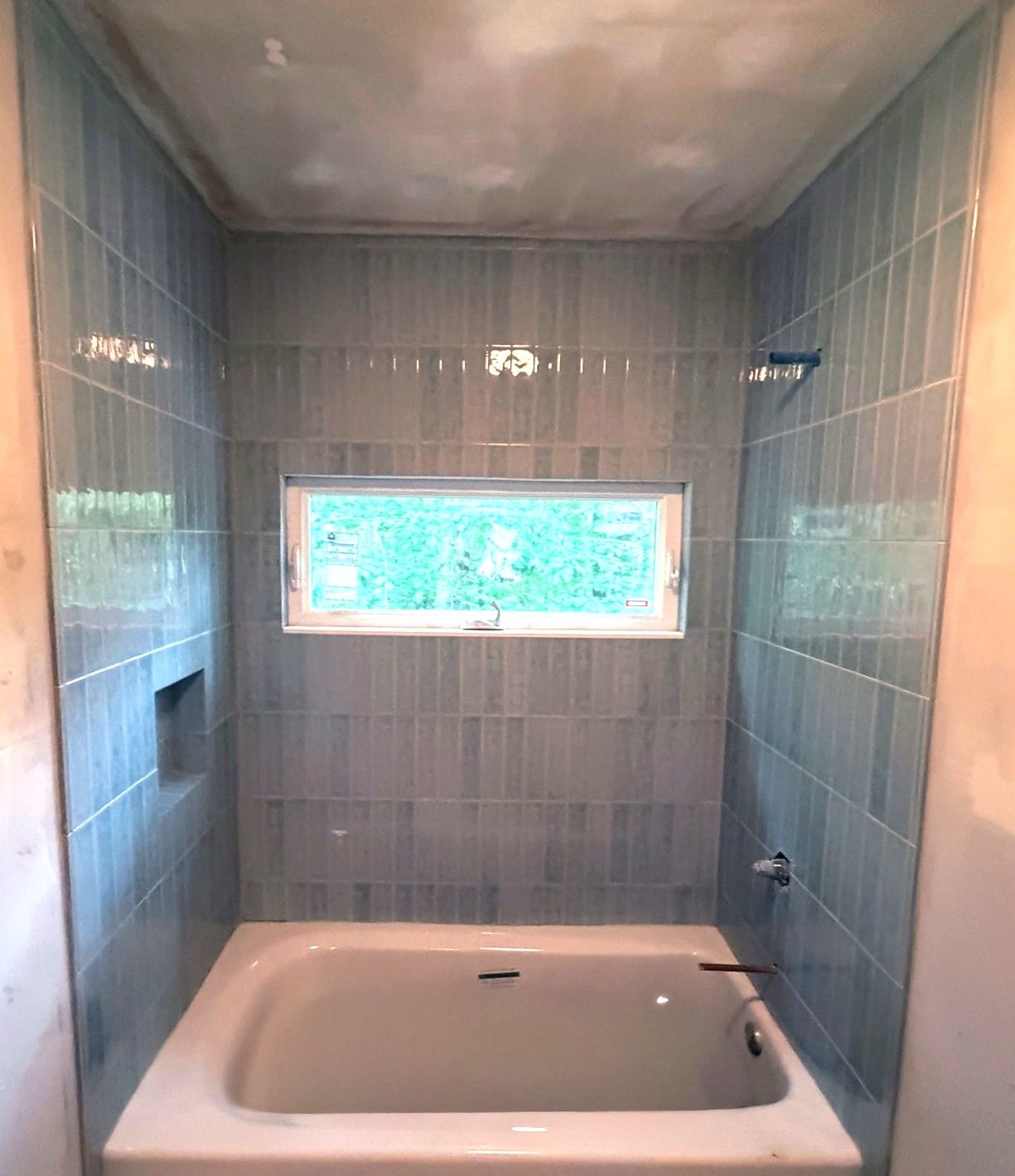 Blue-gray vertical subway tiled bathtub surround with window and built-in niche shelf.