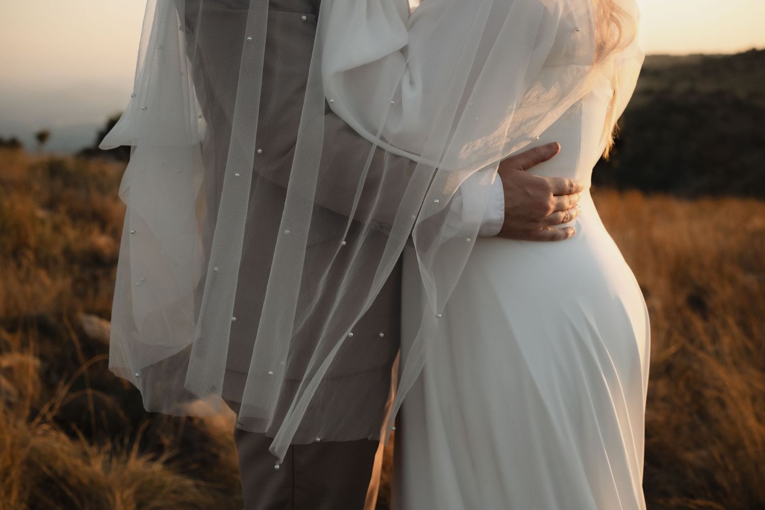 Bride and groom embracing in golden field with pearl wedding veil.