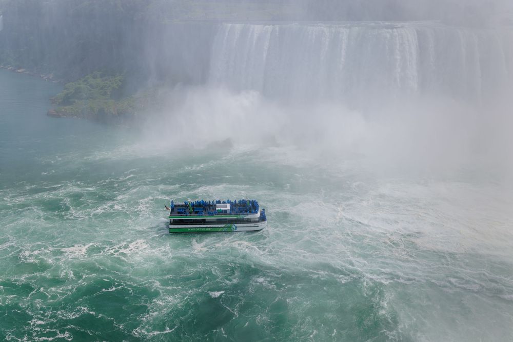 A tour boat navigates the misty turquoise waters near the base of Niagara Falls.
