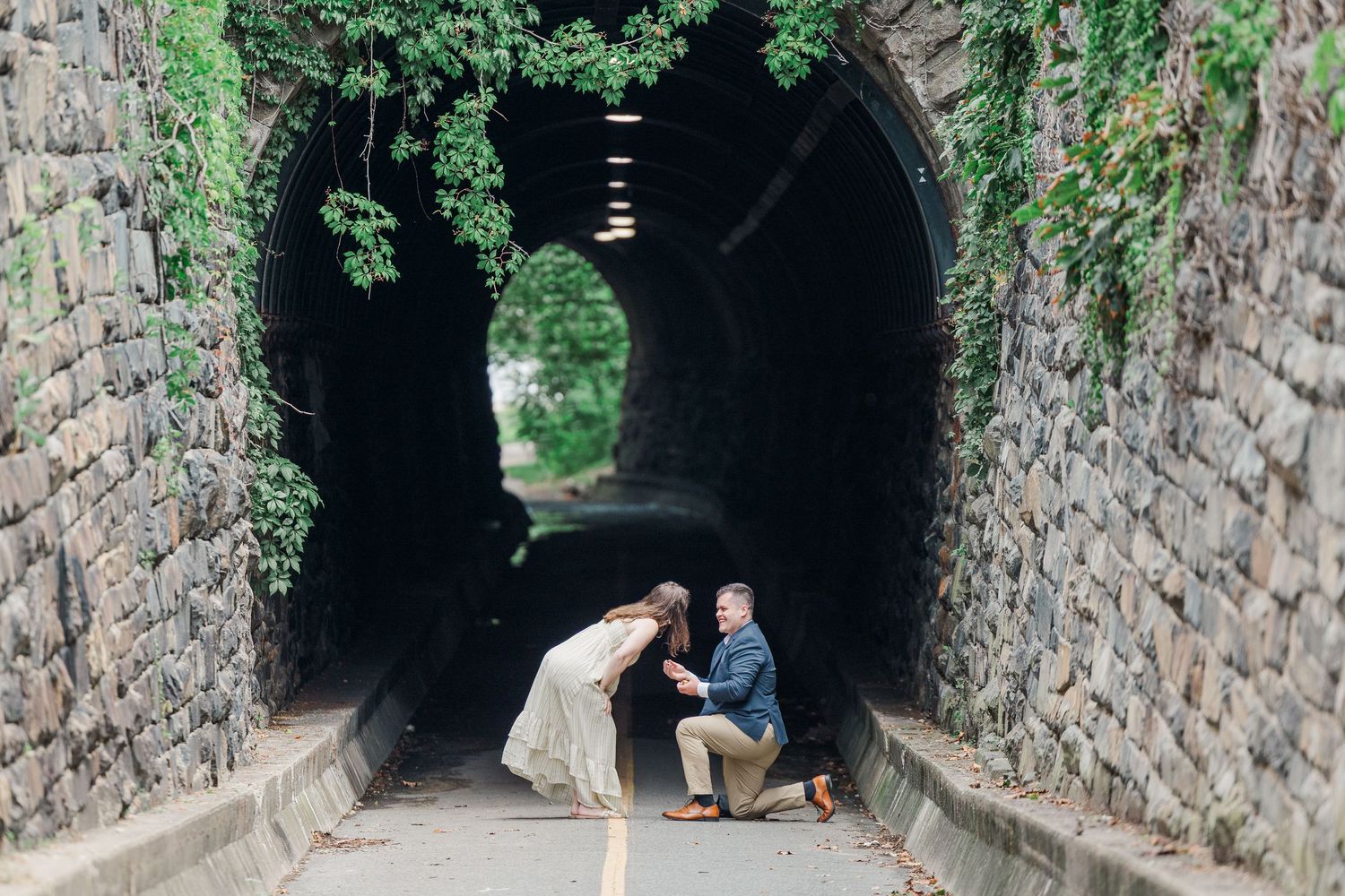 Couple sharing a romantic marriage proposal moment at a stone tunnel entrance covered in lush green ivy.