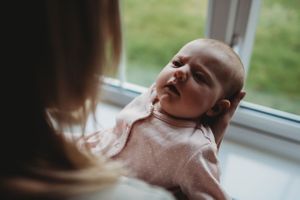 A sweet moment with an infant in pink clothing by a window.