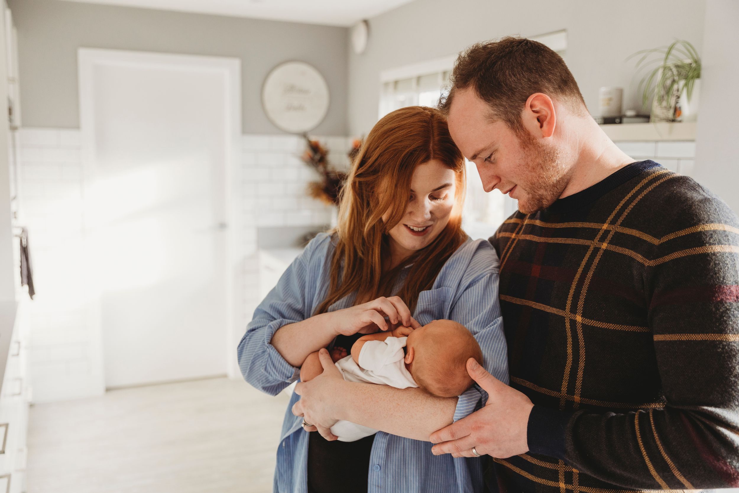 Intimate indoor portrait of parents gazing lovingly at their newborn baby in natural light.