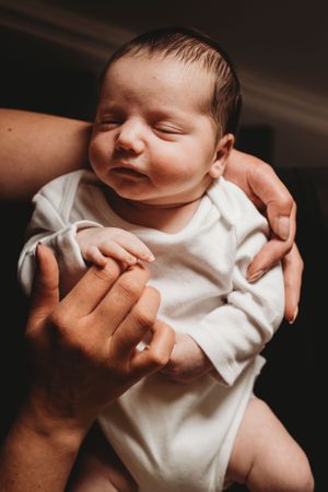 Peaceful sleeping newborn in white onesie cradled in hands.