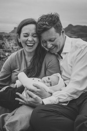 Black and white portrait of family sharing joyful moment with newborn outdoors.
